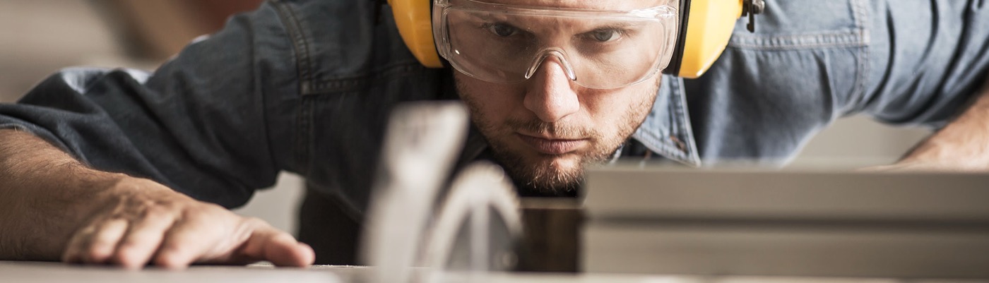 Handwerker mit Schutzbrille und Gehörschutz beim präzisen Zuschnitt von Holz für den Bautenschutz